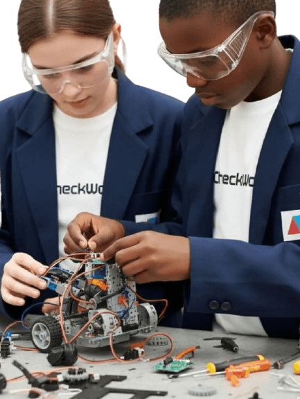 Two students in safety glasses assembling a wired robotics kit